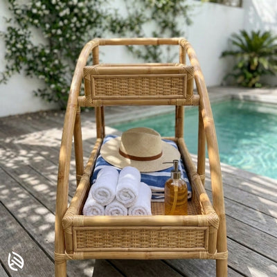 Wicker trolley with towels, a hat, and a bottle by a poolside