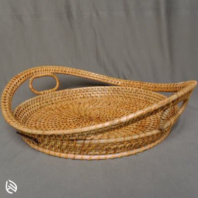 Harvest Hold rattan tray with sculpted curved handles, circular base, and natural cane finish – front angle view