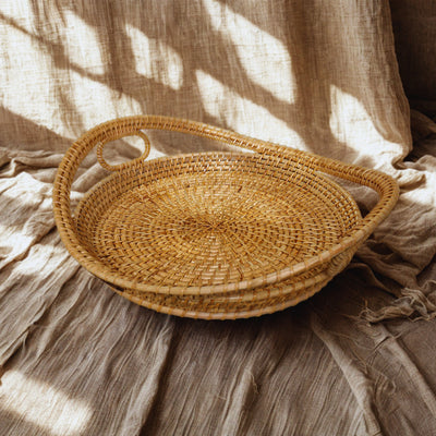 Handwoven circular rattan tray Harvest Hold styled on earthy fabric under sunlight – ideal for home decor or gifting