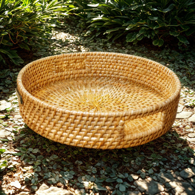 Natural round rattan tray Whisper Weave displayed outdoors on stone path surrounded by foliage