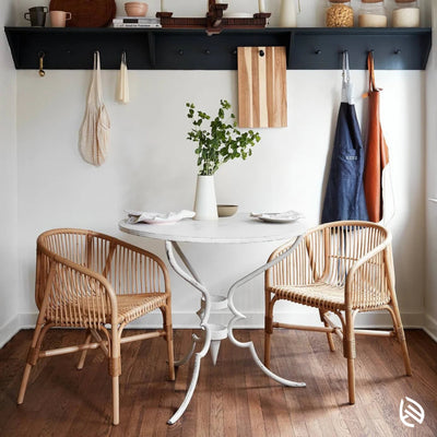 Pair of rattan café chairs around white dining table in cozy kitchen