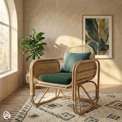 Wicker chair with green cushions in a room with a plant and artwork on the wall.