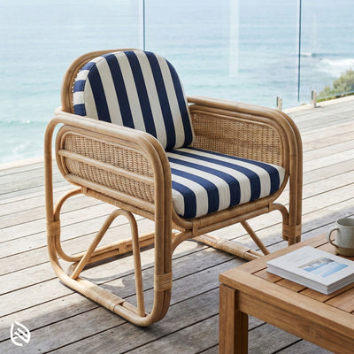 Wicker chair with striped cushion on a wooden deck by the sea